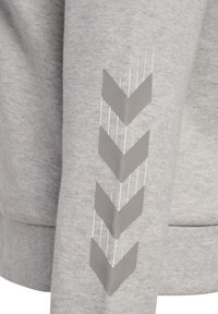 Materiale di felpa grigia con una texture liscia, caratterizzato da un design grafico a zigzag bianco e grigio sulla manica.