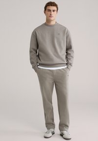 Lysegrå sweatshirt med rund halsudskæring og et lille logo på brystet, kombineret med matchende tilspidsede sweatpants og sneakers.