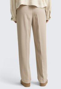 Pantalones beige de pierna ancha con una textura de tela suave, que presentan una cintura de altura media y un diseño simple y limpio. Fondo liso para contraste.