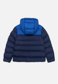 Marineblauwe pufferjack met een contrasterende blauwe capuchon. Gevoerde ontwerp, zonder ritszakken. Zacht, geïsoleerd materiaal, mouwlengte tot halverwege de arm.