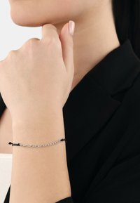 Bracciale in argento con nodi neri, design sottile, indossato al polso, su uno sfondo neutro, che mette in risalto il contrasto e la texture.