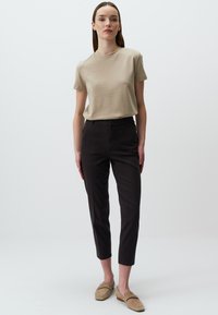 Beżowa koszulka z okrągłym dekoltem, czarne spodnie slim-fit i taupe'owe buty wsuwane. Gładki materiał, dopasowany krój, minimalistyczny design.