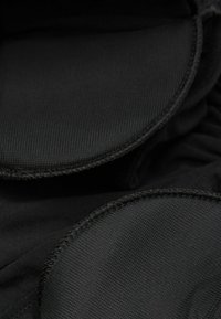 Tissu noir avec une finition texturée, présentant des bords arrondis et des coutures visibles. Le matériau semble flexible et durable.