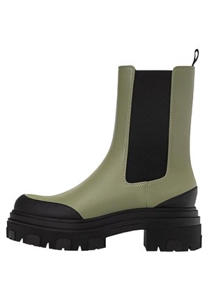 Olive green ankle boot with black elastic side panel, black toe cap, pull tab, and thick textured black sole.