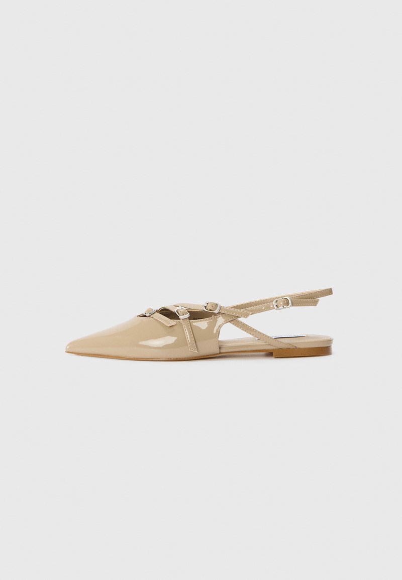 Beige patent leather slingback flats with pointed toe, decorative straps and buckles, and a low heel. Smooth, glossy finish with minimal detailing.