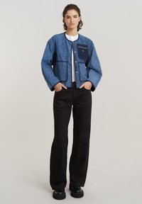 Jachetă bleu matlasată cu accente navy, având guler rotund, nasturi tip snap și două buzunare frontale. Asortată cu pantaloni negri cu picioare late și pantofi.