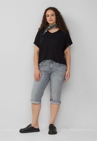 Zwarte V-hals t-shirt, losse pasvorm, gecombineerd met lichtgrijze denim capri's met omslag. Zwarte instap schoenen met decoratieve hardware accenten.