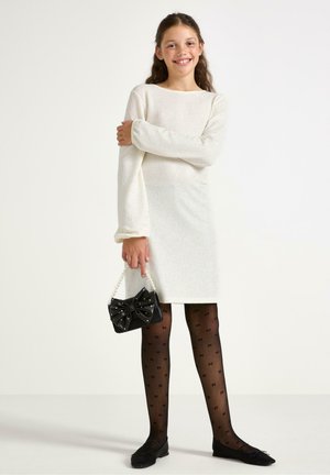 Bíl dress s texturou a dlouhými rukávy; kabelka s černou mašlí; černé punčocháče s vzorem; a černé baleríny. Jednoduchý a elegantní design.