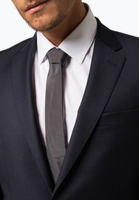 Hochwertige Marineblau strukturierte Anzugjacke mit einer einzelnen Brusttasche, kombiniert mit einem hellen Hemd mit Kragen und einer passenden grauen Krawatte.