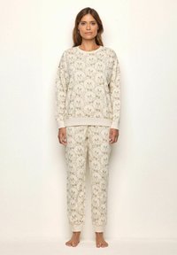 Sudadera beige y pantalones a juego con un patrón repetido de caras de oso. Material suave con puños y cintura acanalados. Ajuste casual.