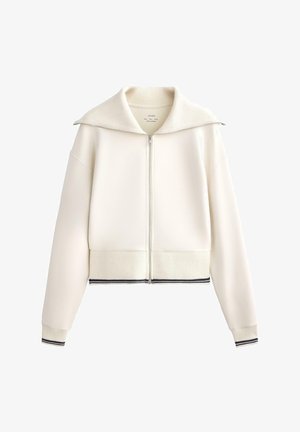 Jachetă albă cu fermoar și guler supradimensionat, cu manșete și tiv zimțat. Are dungi contrastante în nuanța navy la tivul de jos. Textură netedă.