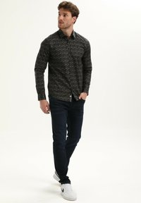Camisa: base oscura con un patrón geométrico; mangas largas, cuello abotonado. Combinada con jeans oscuros y zapatillas blancas.