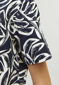 Camicia a maniche corte in tessuto blu navy e bianco, con un audace motivo a foglia in pennellate. Il materiale appare leggero e con una superficie liscia.