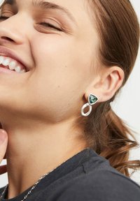 Pendientes de plata con una piedra semipreciosa verde en forma de triángulo y un acento de metal pulido circular. El diseño es minimalista con un acabado elegante.