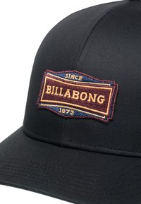 Casquette de baseball noire en tissu texturé, ornée d'un patch brodé coloré avec les détails "BILLABONG" et "DEPUIS 1973".