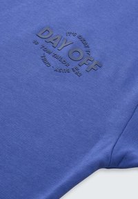 T-shirt in cotone blu con testo in rilievo "DAY OFF" in un design circolare; texture liscia con maniche corte e scollo rotondo.
