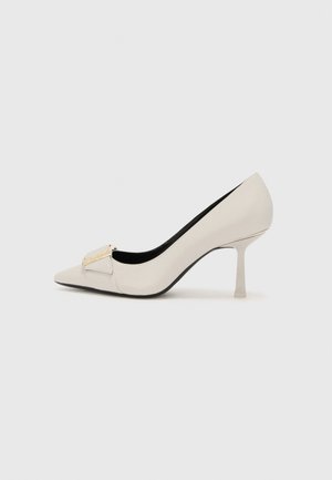 Beige high-heeled pump with a pointed toe, glossy leather material, gold-tone accent detail on the front, and a slender stiletto heel.