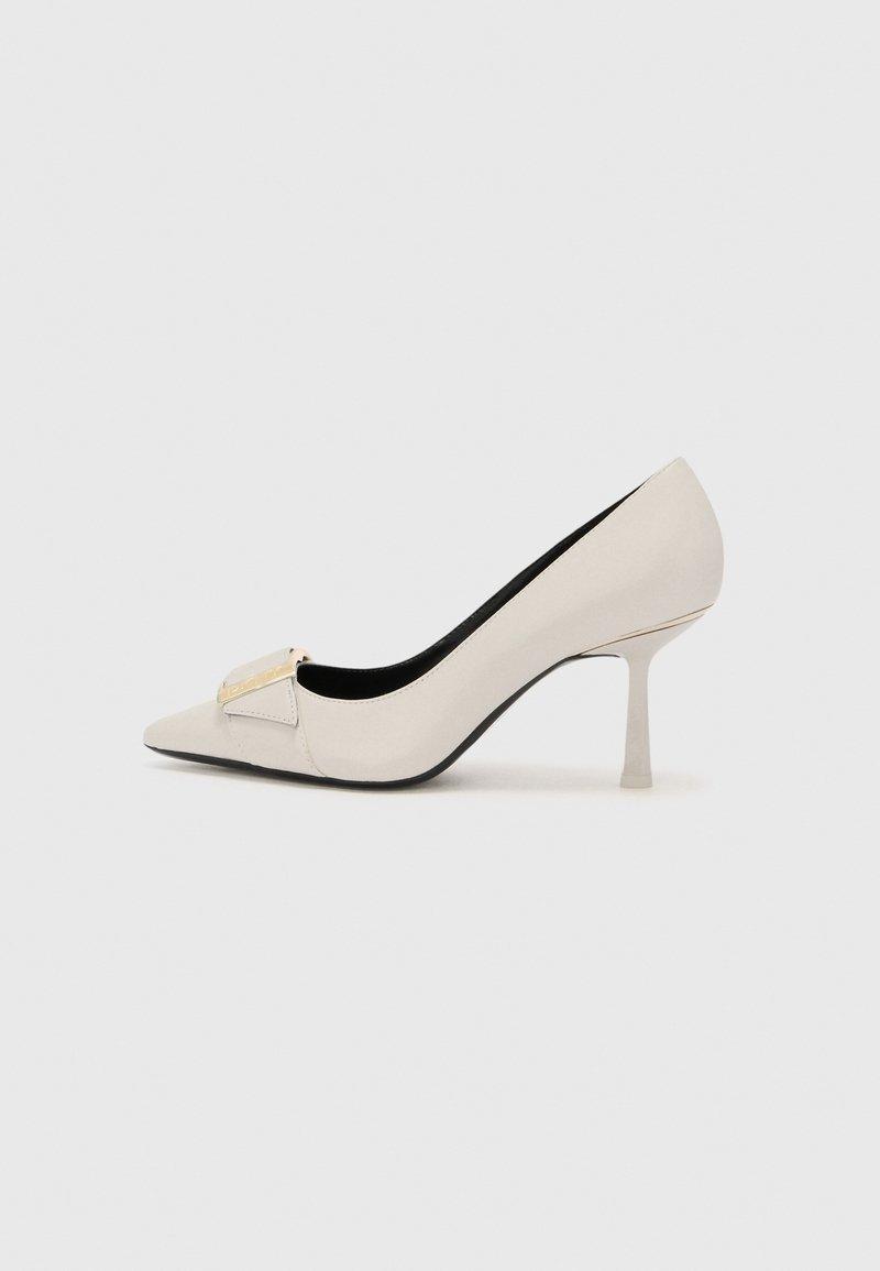 Sandalias de salto alto bege com biqueira pontiaguda, material de couro brilhante, detalhe de acabamento dourado na parte da frente e um salto fino tipo stiletto.