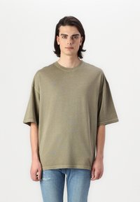 Oliven grøn oversized T-shirt med korte ærmer, rund halsudskæring og en blød tekstur, parret med lyseblå slidte jeans.