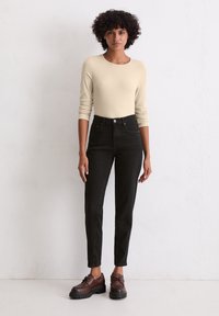 Beżowa bluzka z długim rękawem, zestawiona z czarnymi spodniami o wysokim stanie i brązowymi butami na sznurówki. Prosty design z gładką teksturą i dopasowanym krojem.