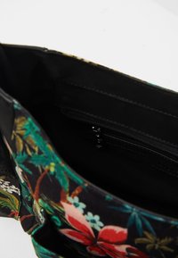 Wnętrze czarnej torby z tkaniny z wielokolorowym kwiatowym wzorem oraz małą kieszonką na zamek wewnątrz.