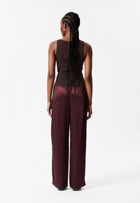 Brauner, gerippter Tanktop kombiniert mit hochgeschnittenen, weit geschnittenen bordeauxroten Hosen; glatte Textur und lockere Passform. Passende Accessoires.