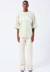 Light green oversized t-shirt with "AROUND THE WORLD" printed in white, paired with cream-colored wide-leg pants and black-and-white sneakers.