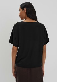 Maglietta nera a maniche corte con una vestibilità comoda, scollatura rotonda e texture liscia, mostrata da dietro su uno sfondo semplice.