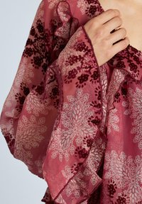 Blusa de chiffon color burdeos con un patrón floral, bordes con volantes y detalles texturizados, confeccionada en un material suave y ligero.