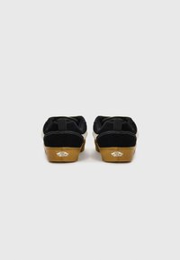 Scarpe in suede nere con suola in gomma color gomma, intersuola bianca e dettagli verdi. Presentano un logo sul tallone e linguette per facilitare l'indossamento.