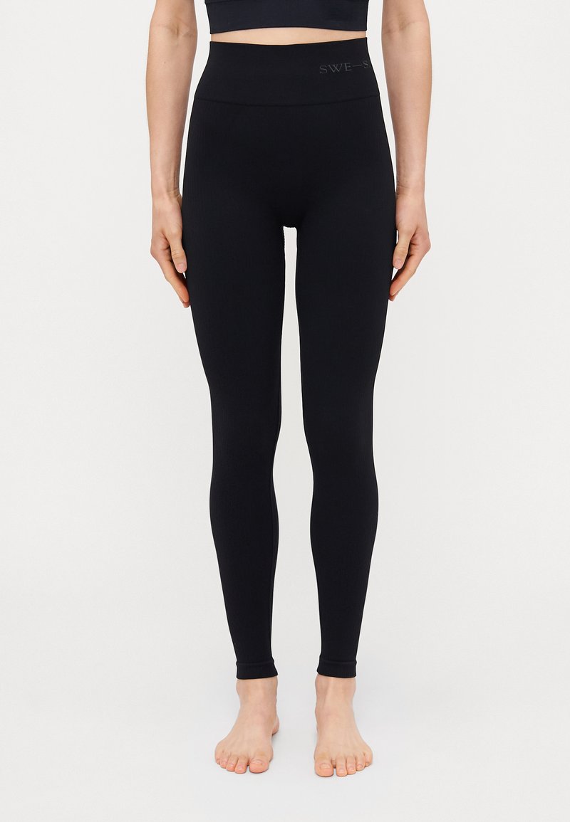 Fekete, magas derekú leggings sima, texturált felülettel, derékpántján logóval és szorosan illeszkedő bokarészekkel.
