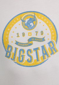 Balta medvilninė marškinėlius su mėlynu ir geltonu apskritimu ir buliuko motyvu, tekstu "BIGSTAR" ir "DIZAINUOTAS EUROPOJE".