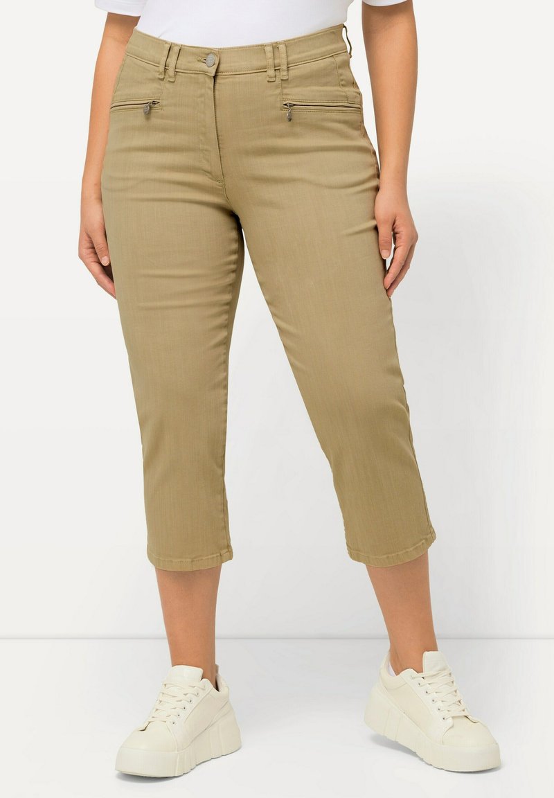 Pantalones recortados beige con bolsillos frontales con cremallera, ajuste slim, hechos de una tela suave. Combinados con zapatillas de plataforma blancas.