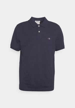 Navy blå polo skjorte laget av bomull. Har en klassisk krage, to-knapps placket og en liten brodert logo på venstre bryst.
