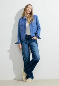 Lichtblauwe cropped jack van gestructureerde stof met twee borstzakken, gecombineerd met wijde donkere denim jeans en crèmekleurige sneakers.