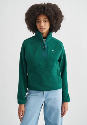 Πράσινο πουλόβερ από φλις με ημίσοληκο γιακά, πλαϊνές τσέπες και λεία υφή. Διαθέτει μικρό λογότυπο στην περιοχή του στήθους.