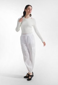 Biały prążkowany długi rękaw w połączeniu z jasnymi lnianymi spodniami cargo i czarnymi balerinami, charakteryzujący się luźnym krojem i elastycznymi mankietami.
