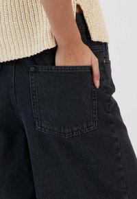 Pantalon en denim noir avec une poche arrière et un haut en tricot texturé beige clair. Comprend une coupe droite et des détails de couture subtils.