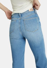 Jeans in denim azzurro chiaro con un design aderente, due tasche posteriori e un'etichetta cucita sulla vita. Il tessuto ha una texture liscia.