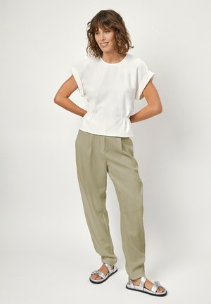 Witte, kortmouwige top met een geraffineerde taille, gecombineerd met lichtgroene, losse broek en zilveren platte sandalen met een strikaccent.