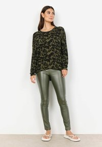 Svart och grönmönstrad långärmad topp som kombineras med åtsittande olivgröna leggings och vita flip-flops. Slät, elastisk tyg.