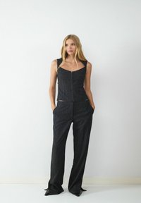 Schwarzes Nadelstreifen-Zweiteiler-Set mit einem figurbetonten, ärmellosen Oberteil mit quadratischem Ausschnitt und passenden, hochgeschnittenen Hosen mit seitlichen Taschen.