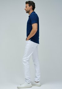 Tummansininen polo-paita lyhyillä hihoilla, yhdistettynä valkoisiin slim-fit-housuihin ja valkoisiin tennareihin. Kankaan pinnassa on tekstuurimainen ulkonäkö.