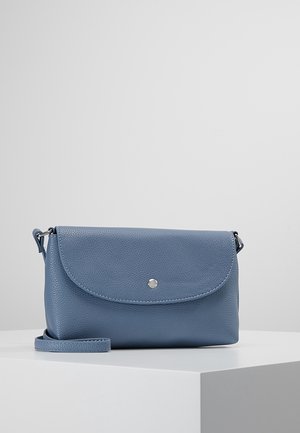 Mała niebieska skórzana torba typu crossbody z klapką i pojedynczym srebrnym guzikiem na białym piedestale na jednolitym szarym tle.
