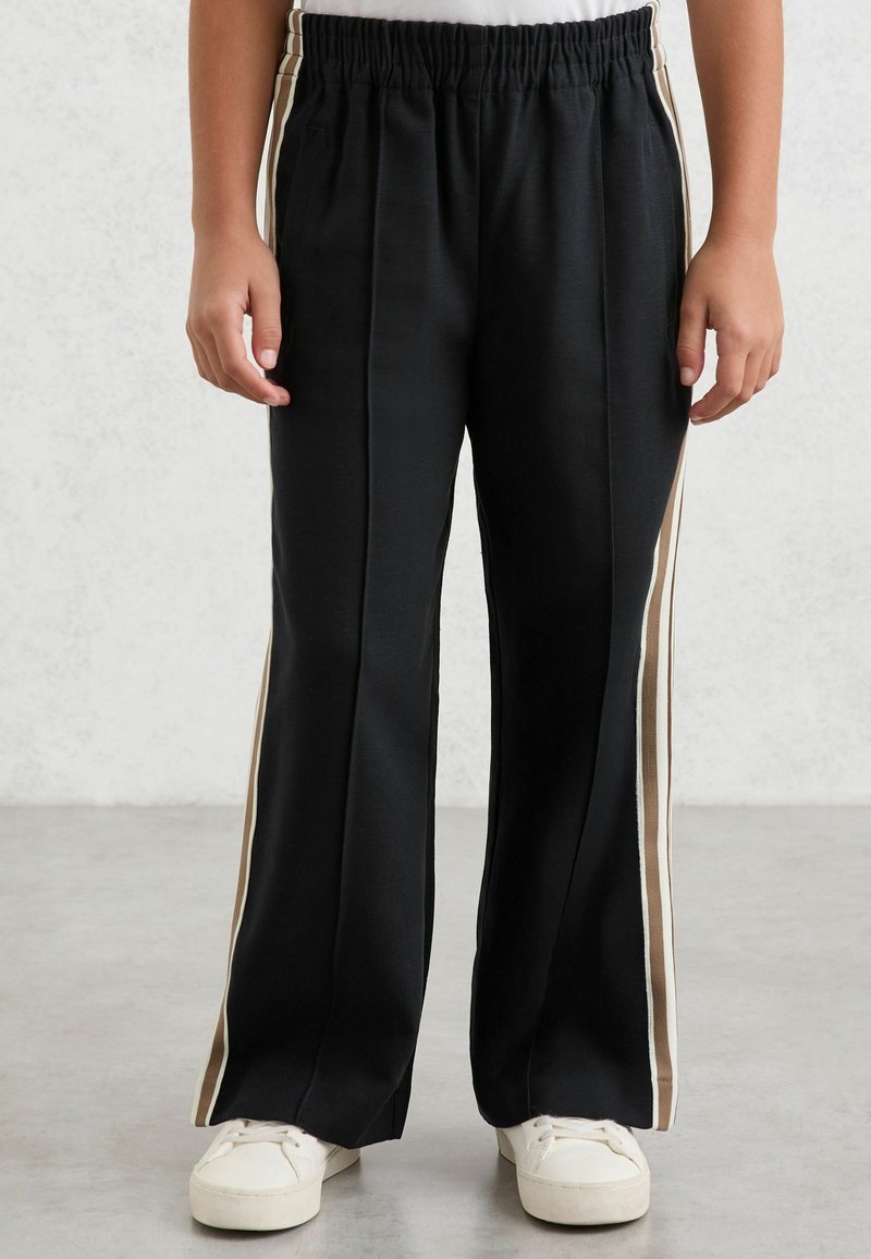 Pantalon de survêtement noir à coupe décontractée, avec une large ceinture, des bandes latérales beige et blanche, et une texture lisse et douce.