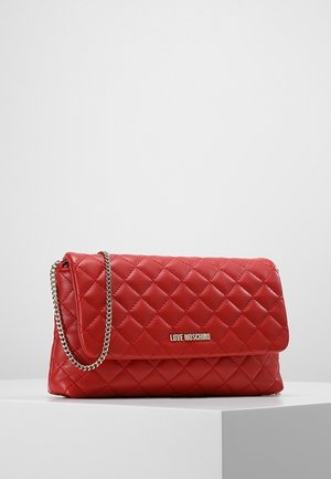 Sac à main en cuir matelassé rouge avec rabat, bandoulière chaîne dorée et logo "Love Moschino" doré sur le devant, posé sur un socle blanc.