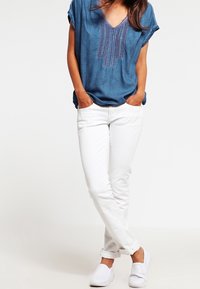 Niebieska denimowa bluzka z dekoltem w serek i krótkimi rękawami, zdobiona haftami. W połączeniu z białymi slim fit spodniami i białymi butami wsuwanymi.