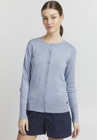 Cardigan bleu clair avec col rond, manches longues et fermeture à boutons. Texture douce, poignets et ourlet côtelés. Détail de petit logo sur le côté inférieur.
