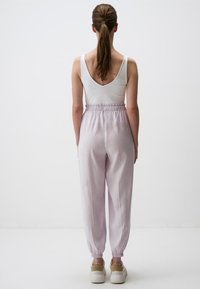 Helllila, hoch geschnittene Jogginghosen mit elastischen Bündchen, aus weichem Stoff. Kombiniert mit einem weißen, ärmellosen Top.
