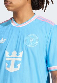 Lyseblå fodboldtrøje med lodrette striber, hvidt logo med en krone og emblem samt rosa detaljer på kraven og ærmerne.